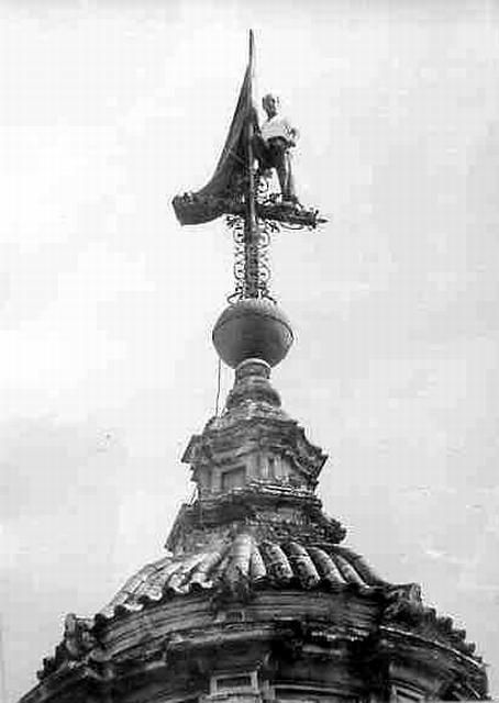Estatua encima de un edificio abovedado sosteniendo una bandera.