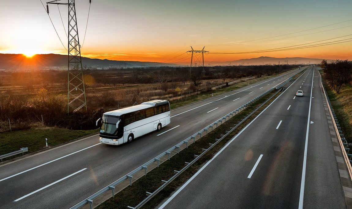 Ein weißer Bus fährt bei Sonnenuntergang eine Autobahn entlang.