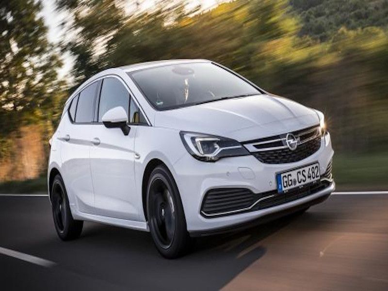 Un Opel Astra hatchback blanco circulando por una carretera, con árboles borrosos en el fondo.