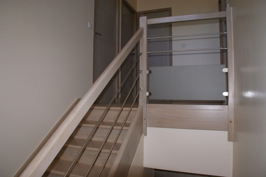 Escalier avec rampes en bois, barres horizontales en métal et panneau en verre dépoli, vu du bas de l'escalier.