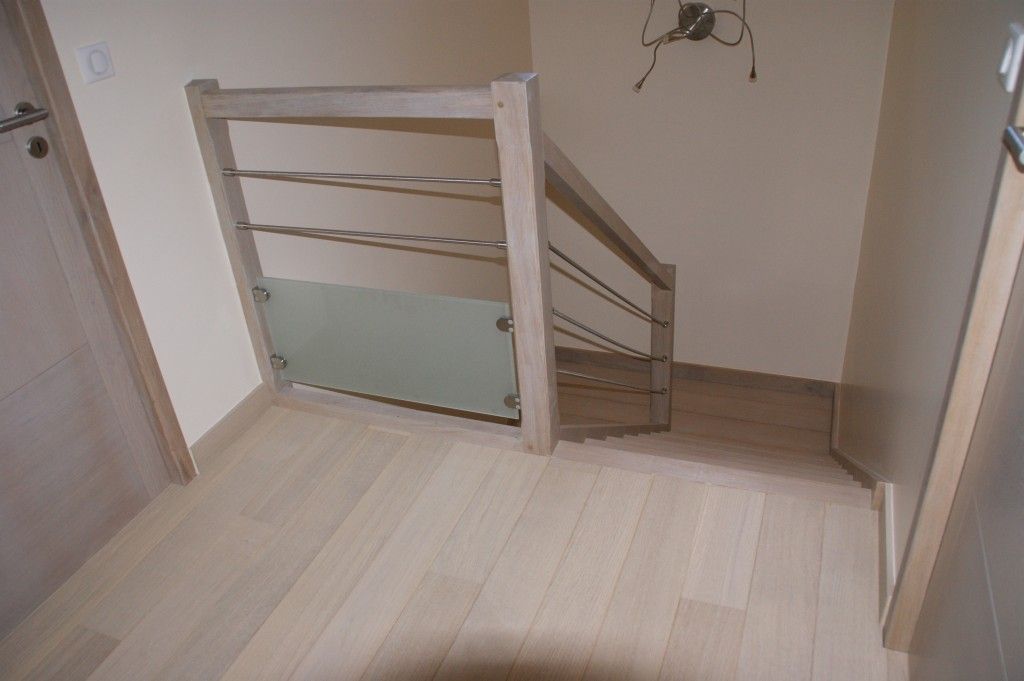 Un escalier en bois clair doté d'une rampe moderne avec des barres horizontales en métal et un panneau inférieur en verre dépoli.