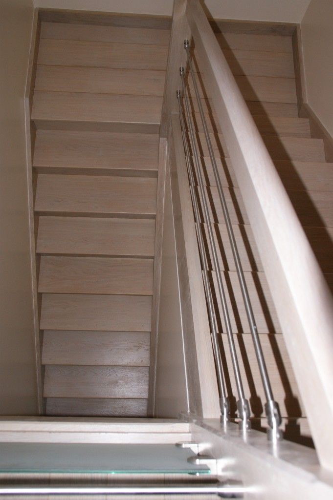 Un escalier en bois clair vu du haut, doté d'une rampe moderne à balustres métalliques.