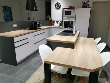 Cuisine moderne avec des armoires blanches et gris foncé, un îlot central avec un comptoir en bois clair et une table assortie.