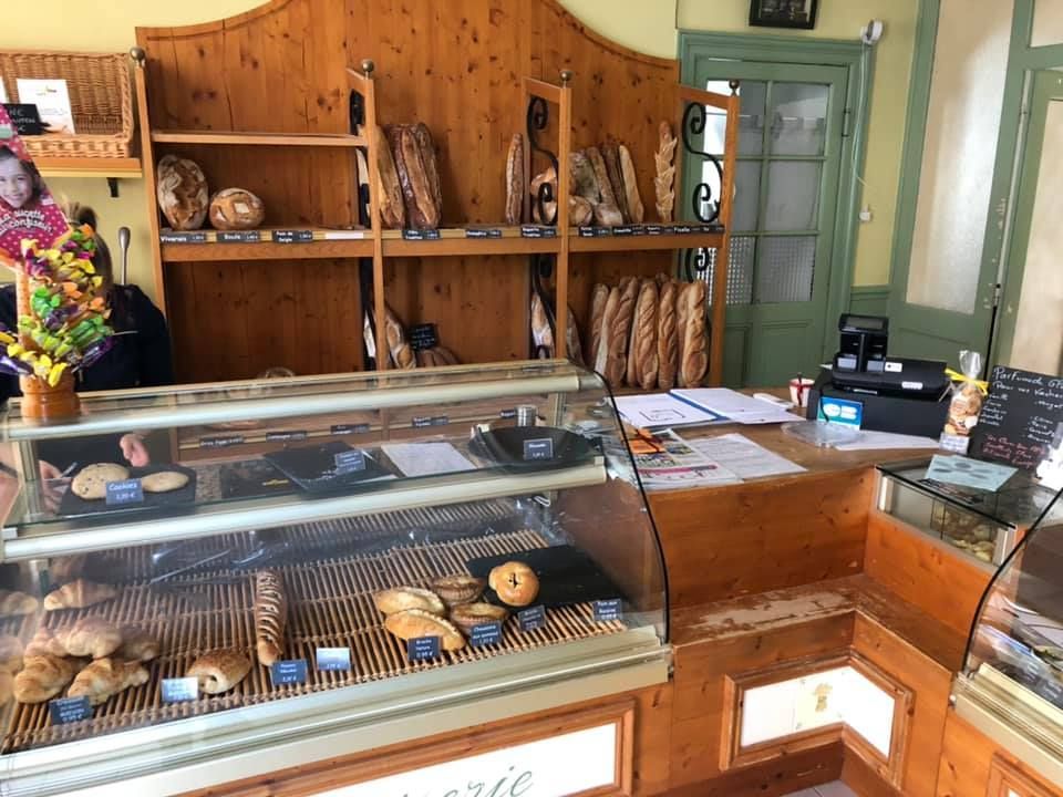 L'intérieur d'une boulangerie rustique avec une vitrine remplie de pâtisseries et des étagères en bois chargées de pain.