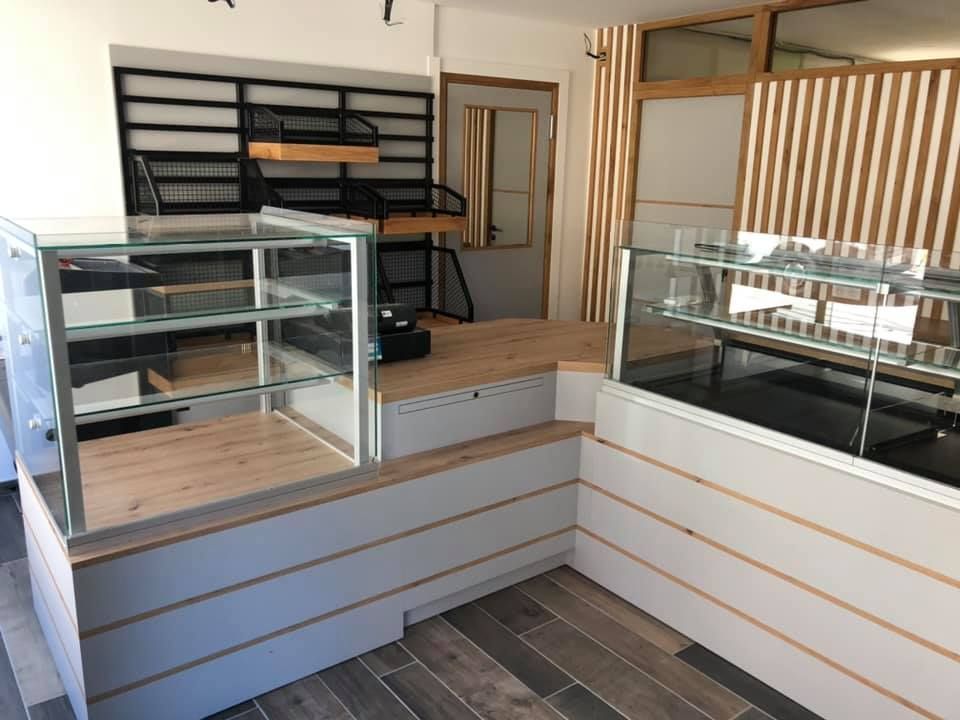 Comptoir de boulangerie vide avec surfaces en bois, vitrines et étagères en métal noir contre un mur en bois à lattes.