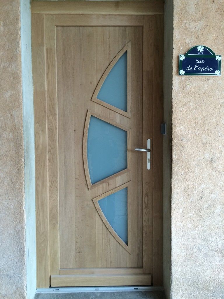 Une porte d'entrée en bois avec trois fenêtres en verre dépoli en forme de croissant, adjacente à une plaque nominative bleue sur un mur texturé.