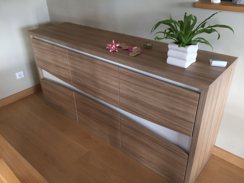 Une commode en bois à deux rangées de tiroirs, surmontée d'une plante en pot et de petits objets décoratifs, dans une chambre.