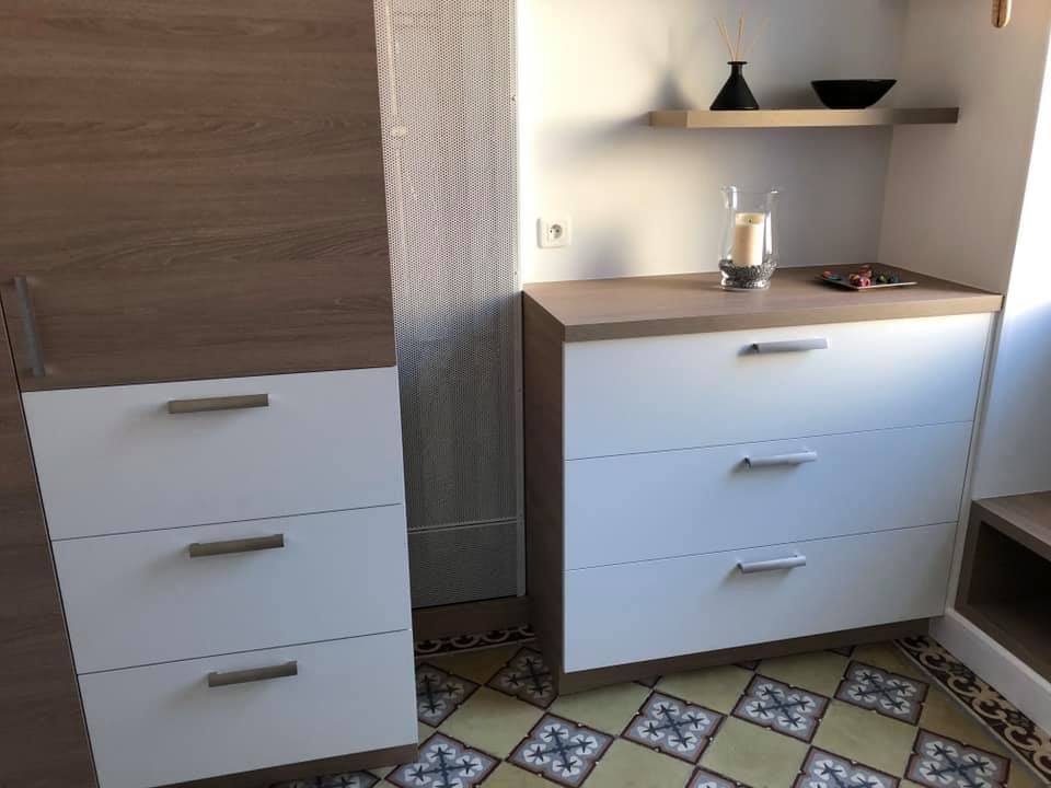 Une commode blanche et boisée ainsi qu'un meuble assorti se dressent sur un sol carrelé à motifs, devant un mur blanc.
