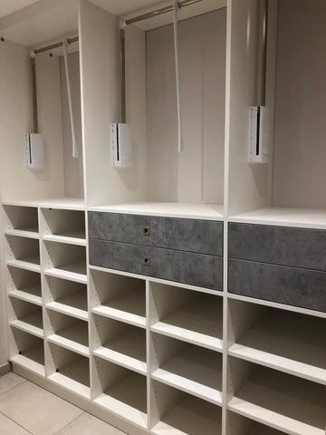 Système d'étagères blanches pour placard avec compartiments ouverts, tringles de suspension et deux ensembles de tiroirs gris.