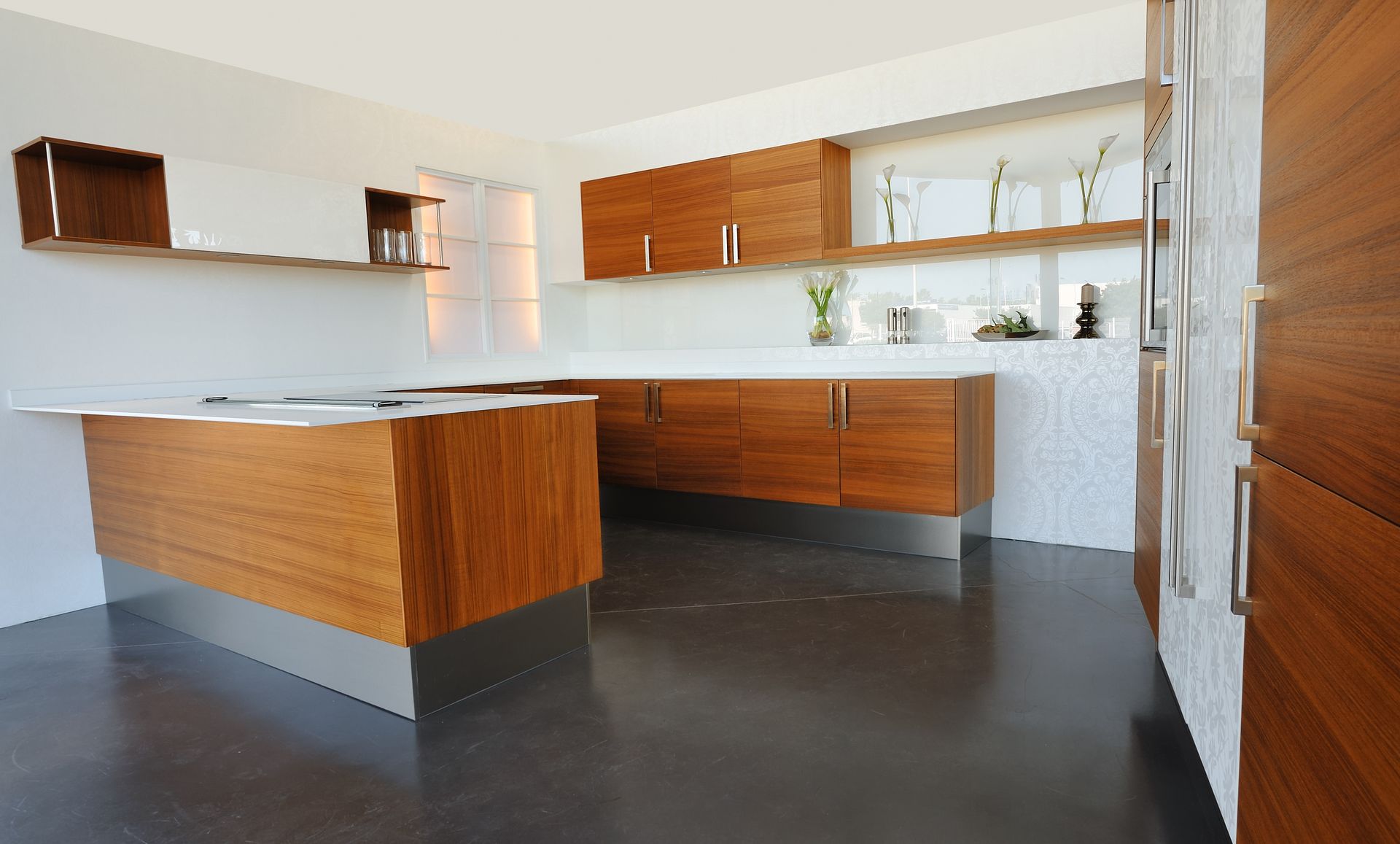 Une cuisine moderne avec des armoires en bois, un îlot central, des comptoirs blancs et un sol foncé poli.