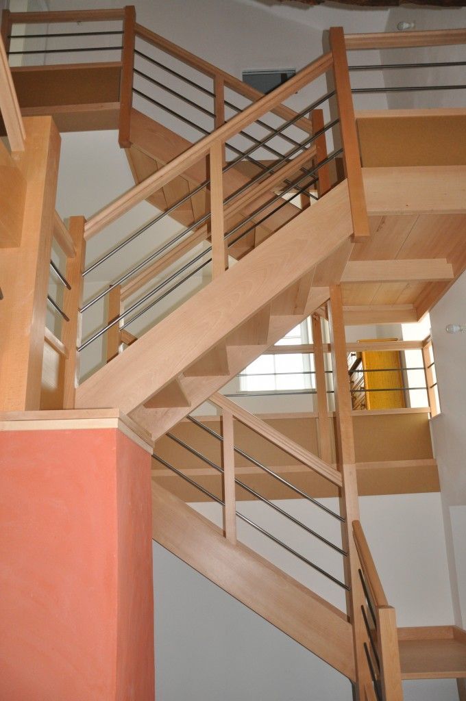 Un escalier à plusieurs niveaux avec des marches en bois clair et des rampes composées de fines barres métalliques horizontales.