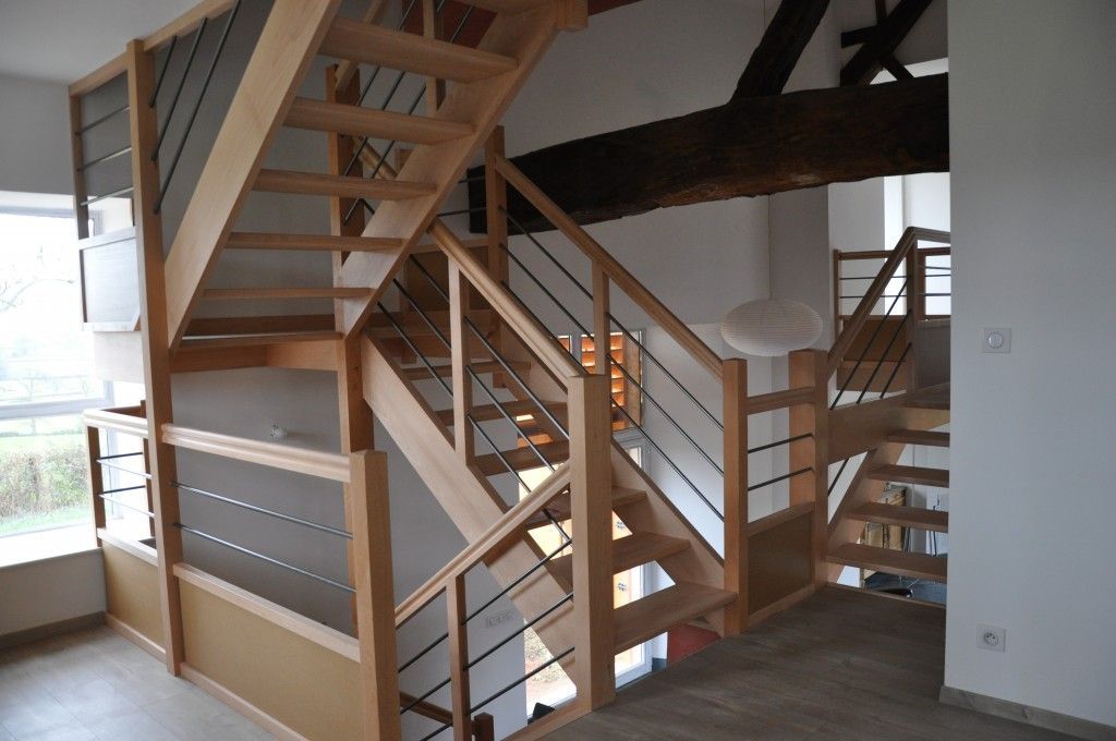 Escalier moderne en bois avec rampes métalliques dans un loft à aire ouverte aux murs blancs et poutres apparentes au plafond.