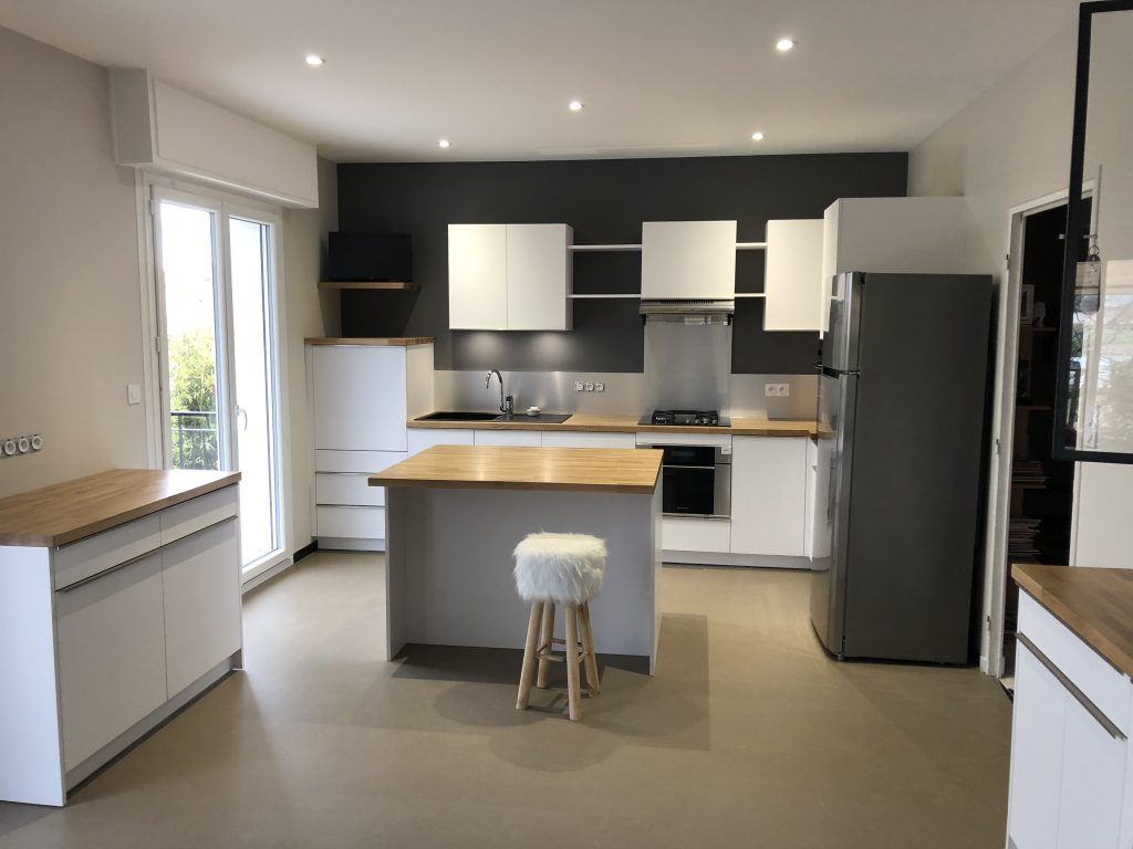 Cuisine moderne avec armoires blanches, comptoirs en bois, un îlot central avec tabouret et un réfrigérateur en acier inoxydable.