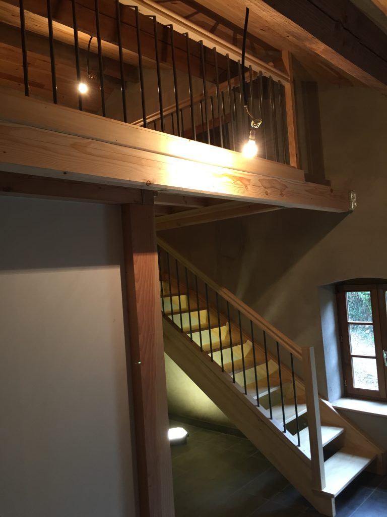 Un escalier en bois avec des rampes en métal noir mène à une mezzanine dotée de rampes assorties et de deux suspensions lumineuses.
