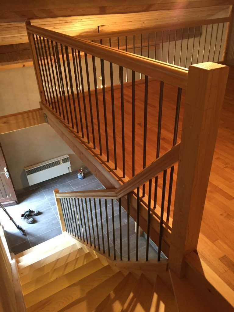 Un escalier en bois et une mezzanine avec des garde-corps composés d'une structure en bois et de fines barreaux verticaux sombres.