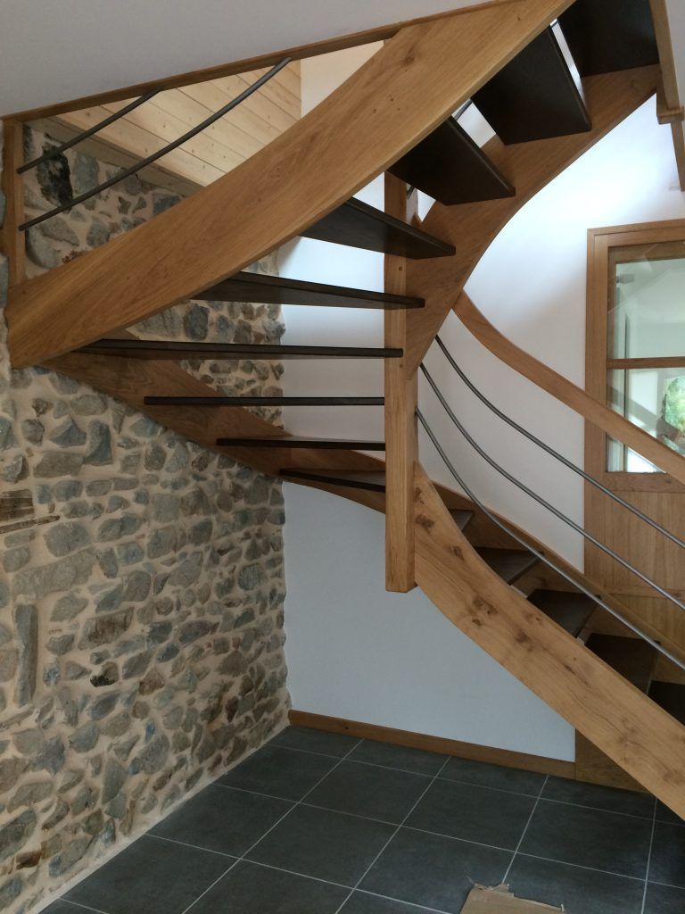 Escalier en bois avec rampes métalliques à l'intérieur d'une pièce avec un mur en pierre et un sol carrelé foncé.