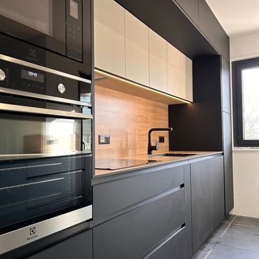 Cuisine moderne avec des armoires blanches et gris foncé, un îlot central avec un comptoir en bois clair et une table assortie.