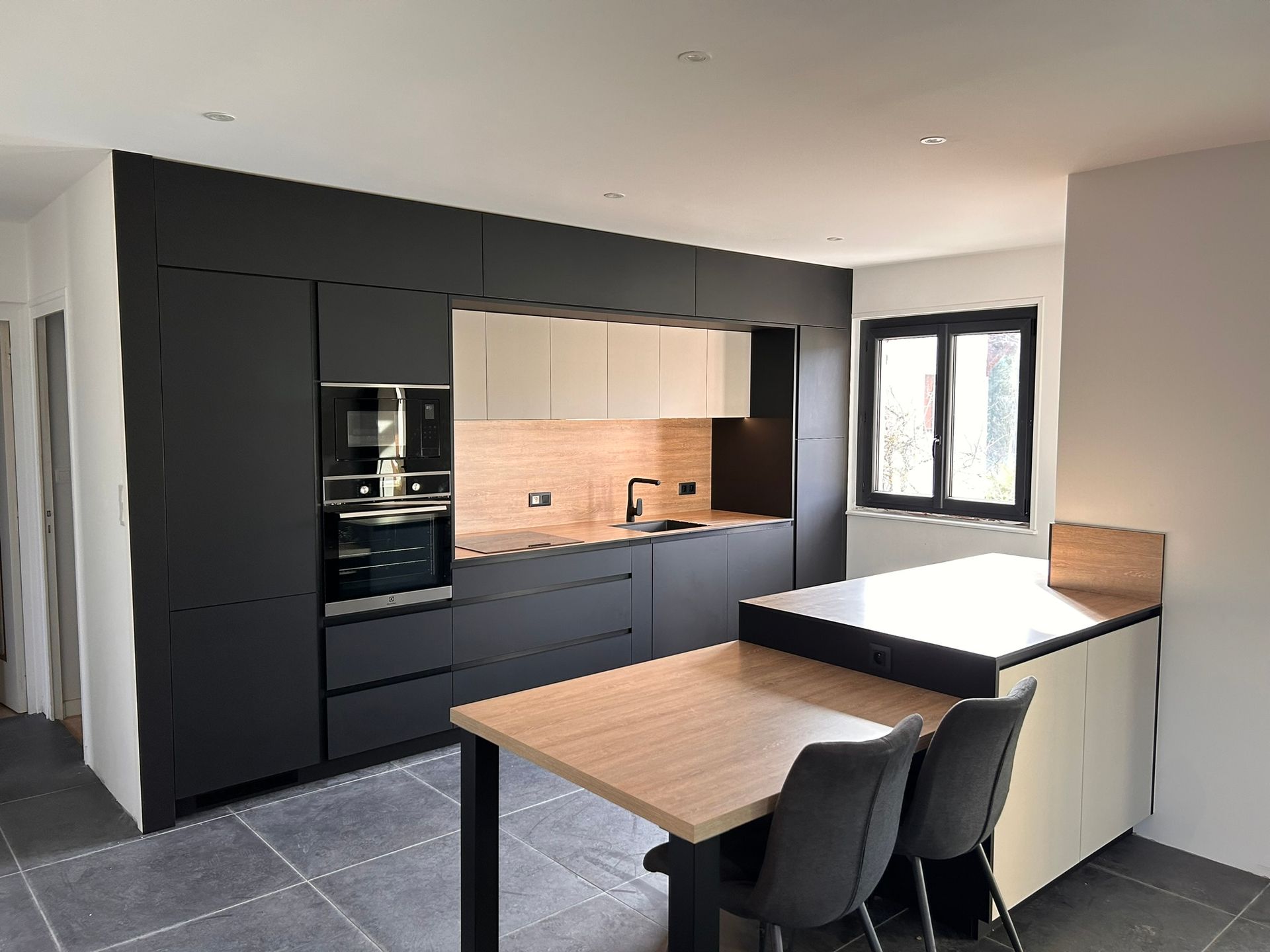 Une cuisine moderne avec des armoires blanches, des comptoirs couleur bois, des touches de gris foncé et une table à manger avec des chaises blanches.