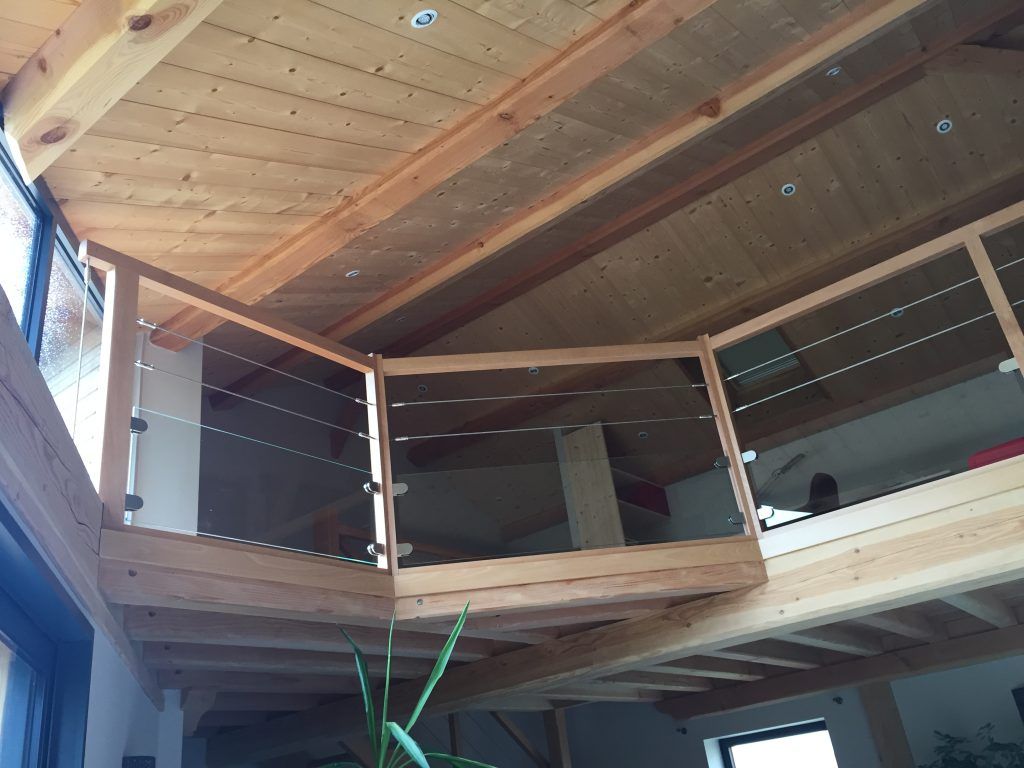 Une mezzanine en bois avec un système de garde-corps à câbles, donnant sur un espace intérieur avec des poutres de plafond en bois.