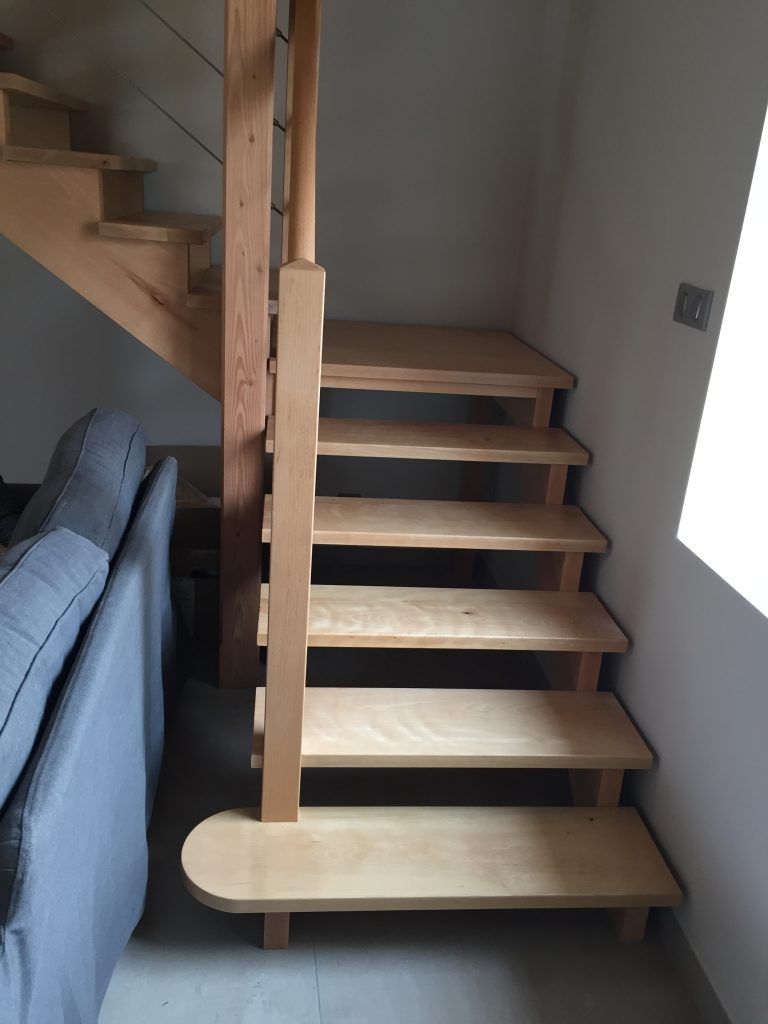 Escalier en bois clair à contremarches ouvertes, avec une marche inférieure arrondie et une rampe assortie.