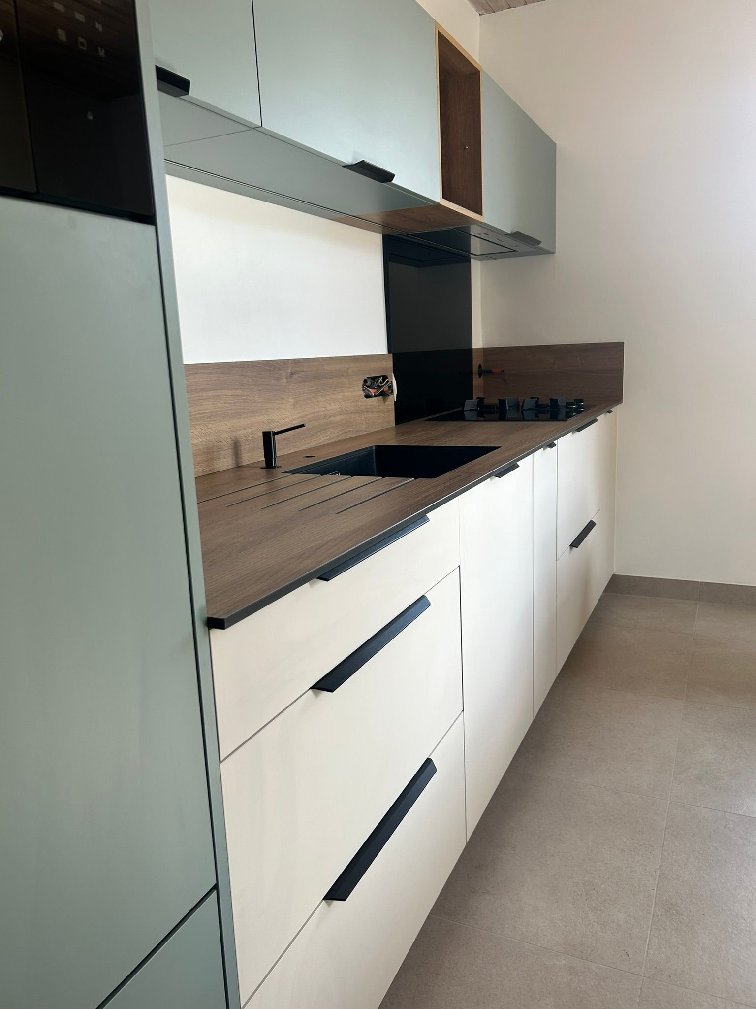 Une cuisine moderne avec des armoires blanches, des comptoirs couleur bois, une cuisinière noire et un évier noir assorti.