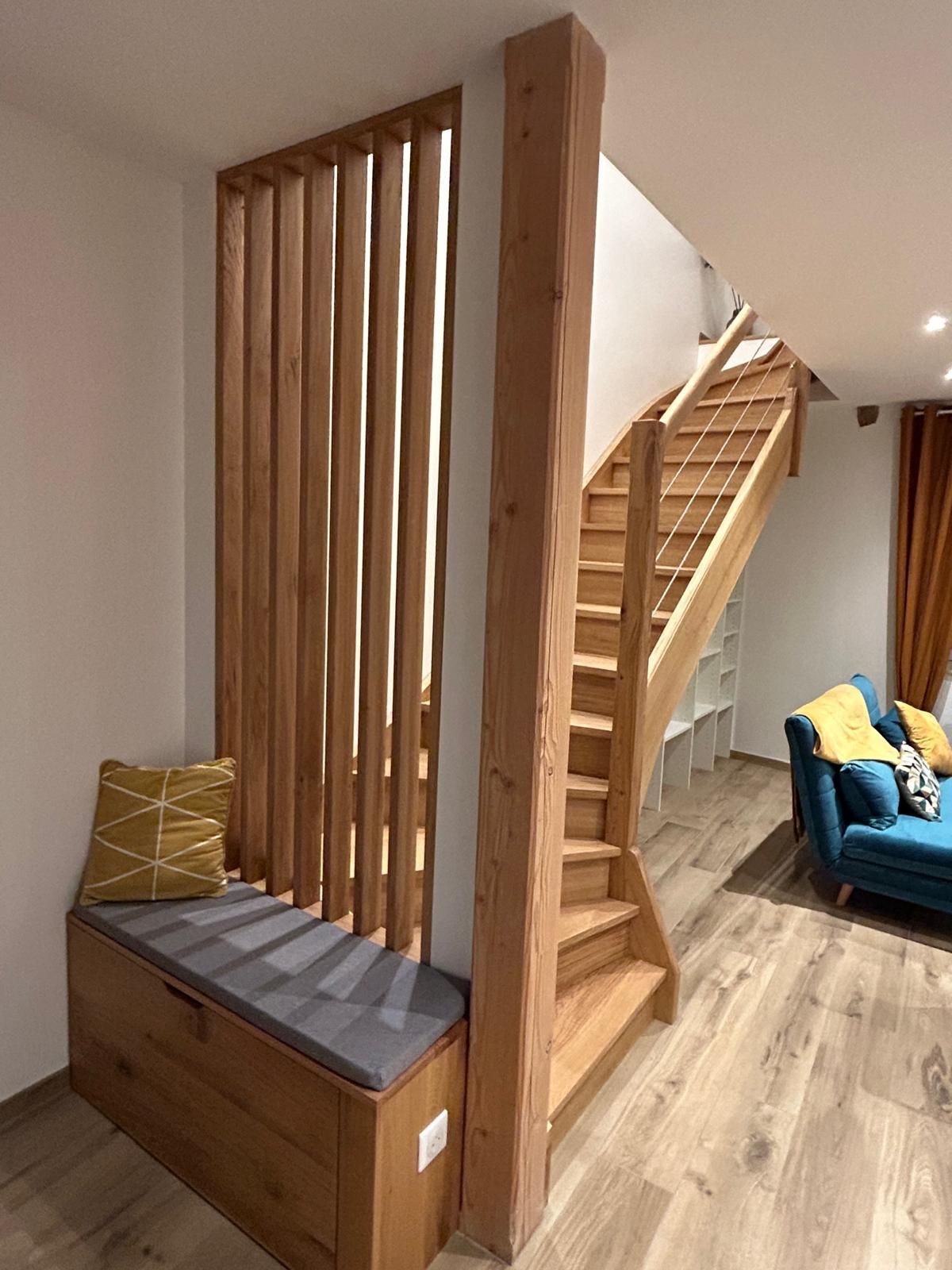Un escalier en bois jouxte une cloison vitrée à cadre en bois, dans une pièce au sol carrelé.