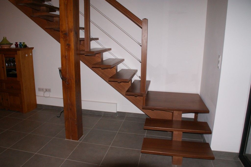 Un escalier en bois avec une rampe en câble dans une pièce au sol carrelé et avec une armoire en bois.