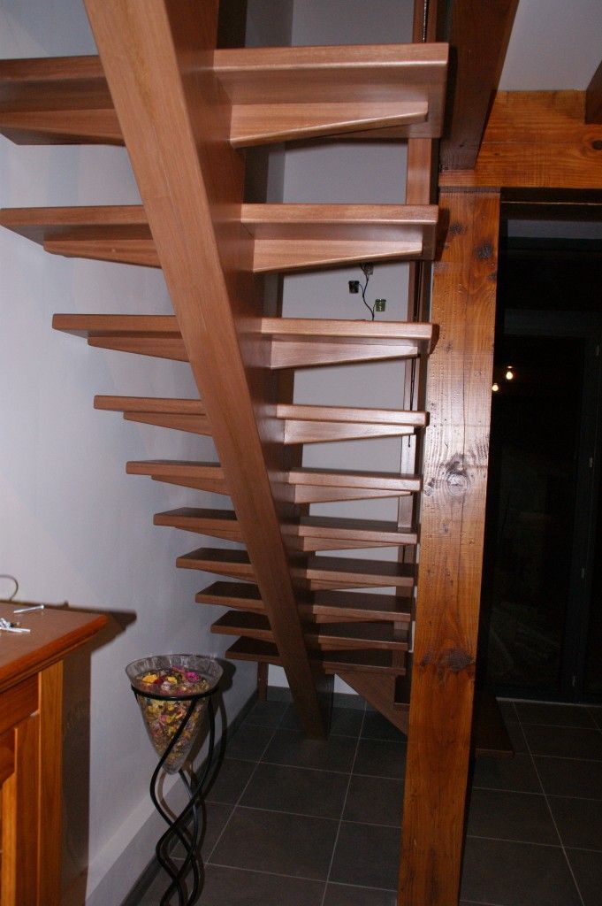 Escalier en bois à marches ouvertes dans une maison, avec une poutre de soutien inclinée et un panier métallique sur un support à la base.
