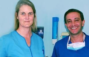 Un hombre y una mujer están parados uno al lado del otro y sonriendo. El hombre lleva una máscara.