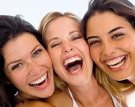Tres mujeres se ríen juntas con la boca abierta.