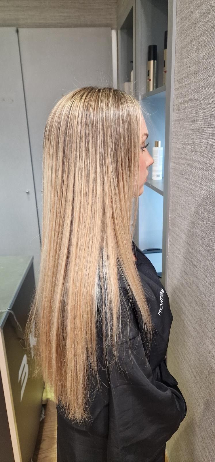 Vista de perfil de una mujer con cabello rubio largo de pie en un pasillo cerca de una pantalla montada en la pared.