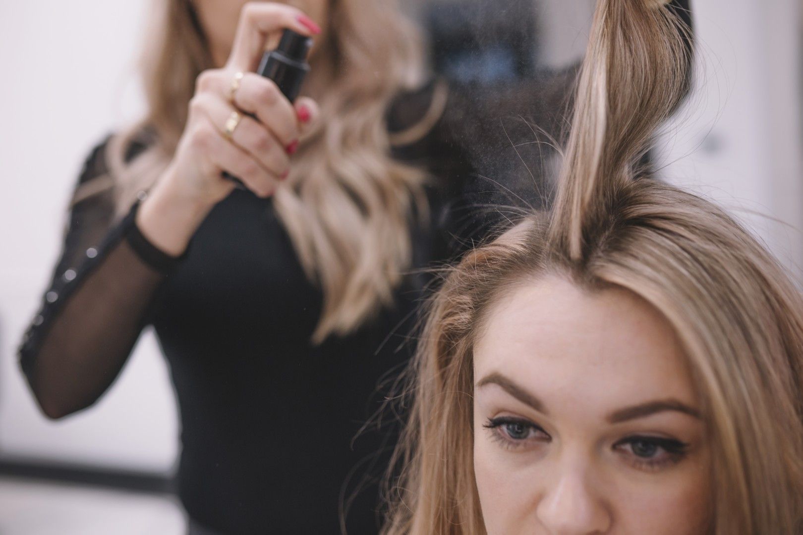 Estilista rociando el cabello de una clienta rubia en un salón de belleza.