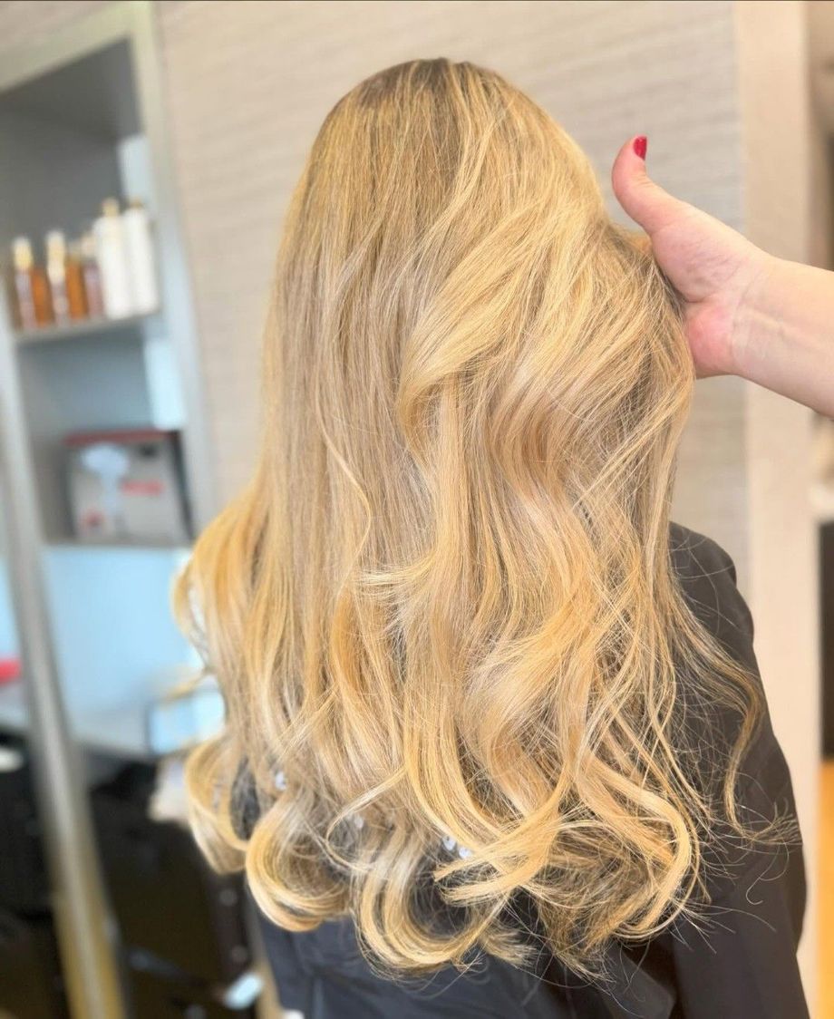 Cabello rubio ondulado peinado en una peluquería, con una mano sujetando el cabello cerca de la coronilla.