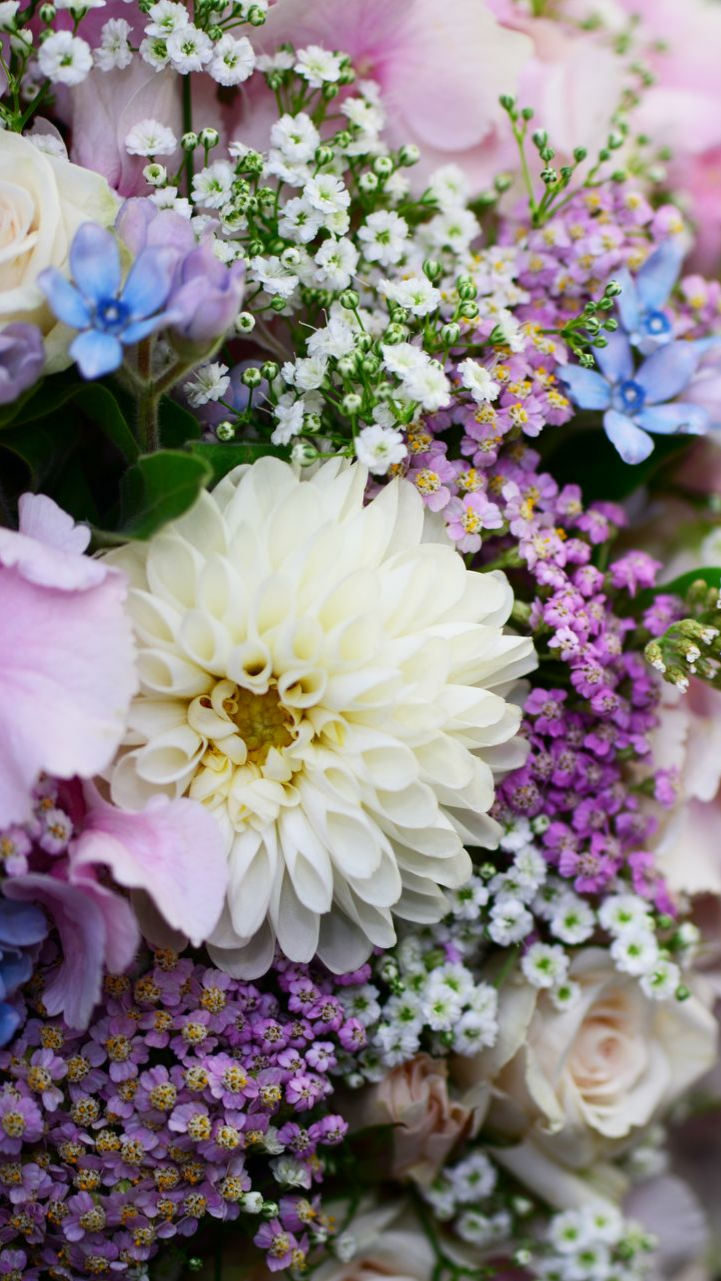 Gros plan d'un bouquet avec un dahlia blanc, des fleurs lavande et bleues et de petites fleurs blanches.