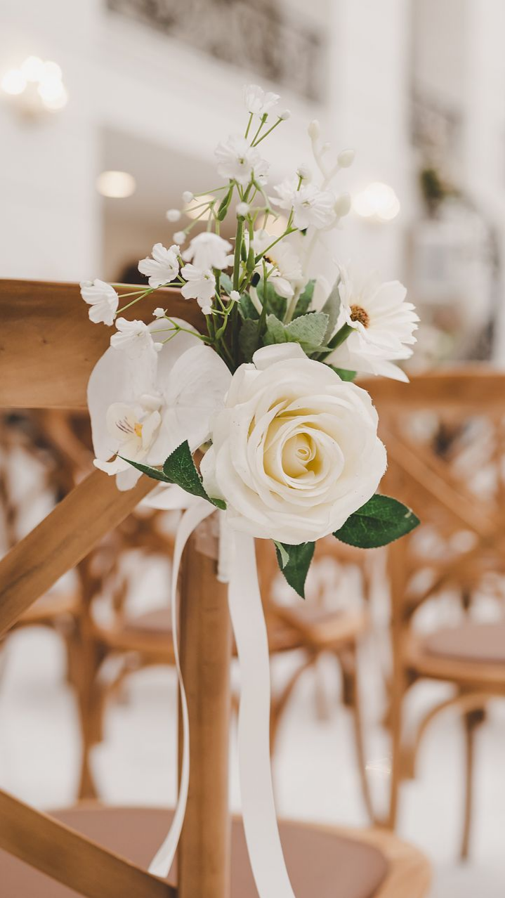 Composition florale blanche sur une chaise en bois, probablement pour une cérémonie de mariage.