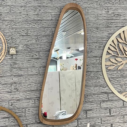 Un miroir asymétrique à cadre en bois accroché à un mur de briques, reflétant une pièce avec des fleurs.