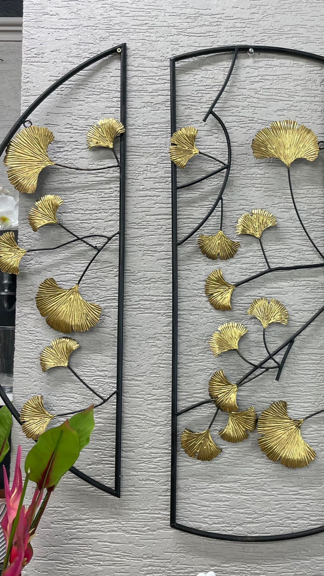 Art mural en métal noir avec des accents de feuilles d'or sur un mur gris texturé.