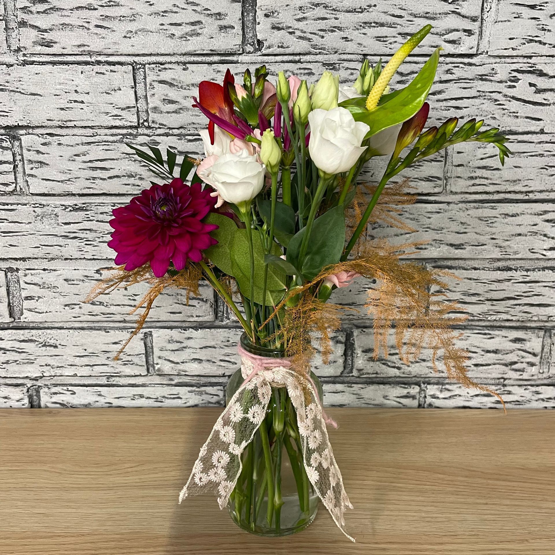 Bouquet de fleurs dans un vase en verre noué avec un ruban de dentelle, sur un fond en briques.