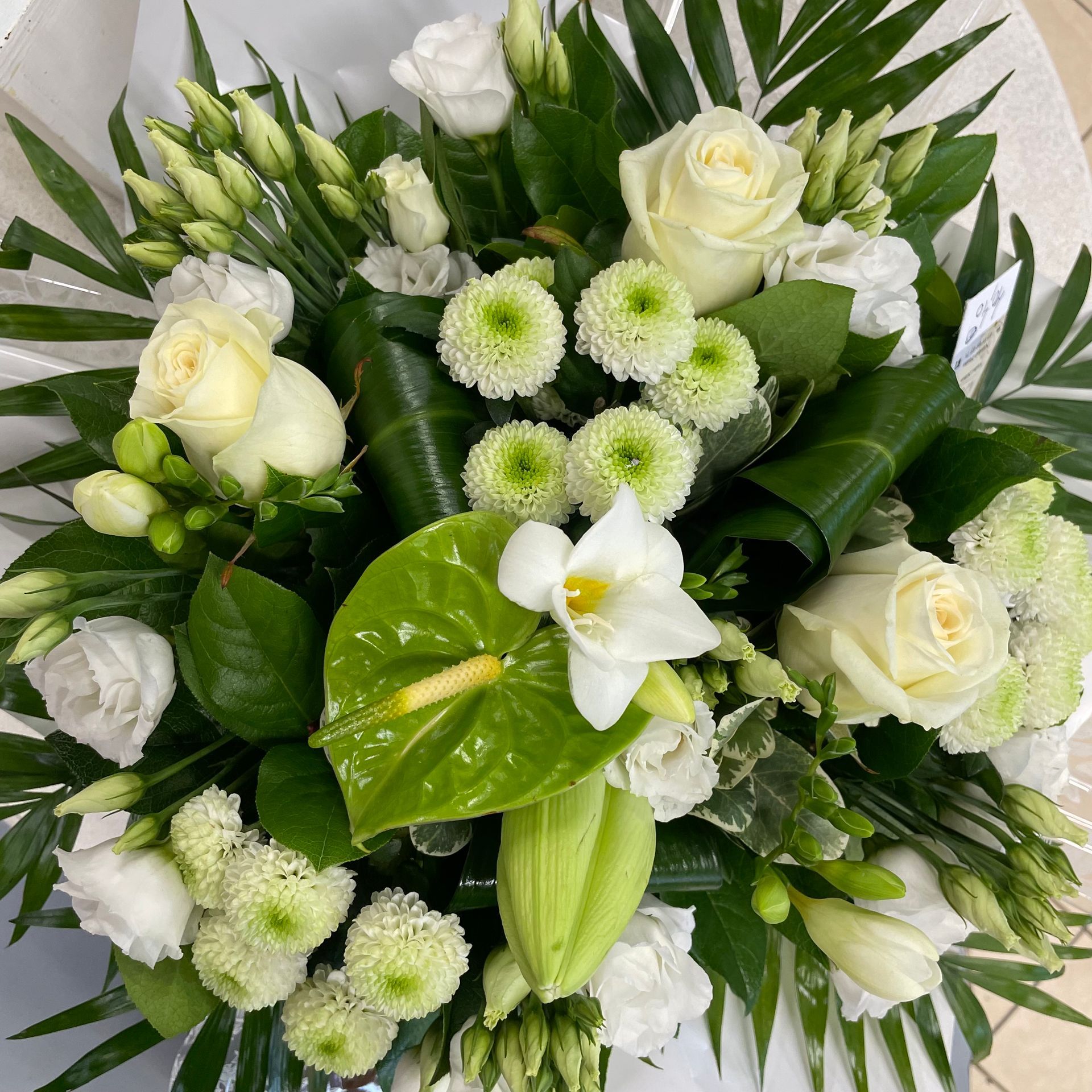 Bouquet de roses blanches, d'anthurium vert et d'autres fleurs blanches et vertes, emballé.