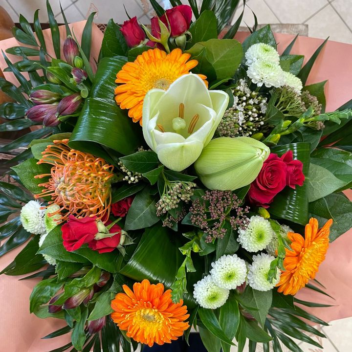 Bouquet de gerberas orange, de roses rouges, d'une tulipe blanche et d'autres fleurs et verdures assorties, emballées dans du papier rose.