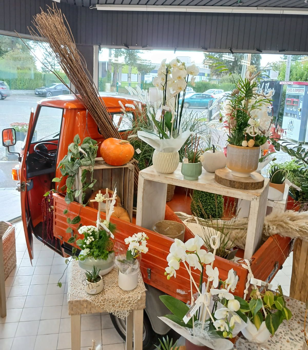 Présentoir de camion fleuri orange avec orchidées, citrouilles et éléments en bois dans une vitrine.