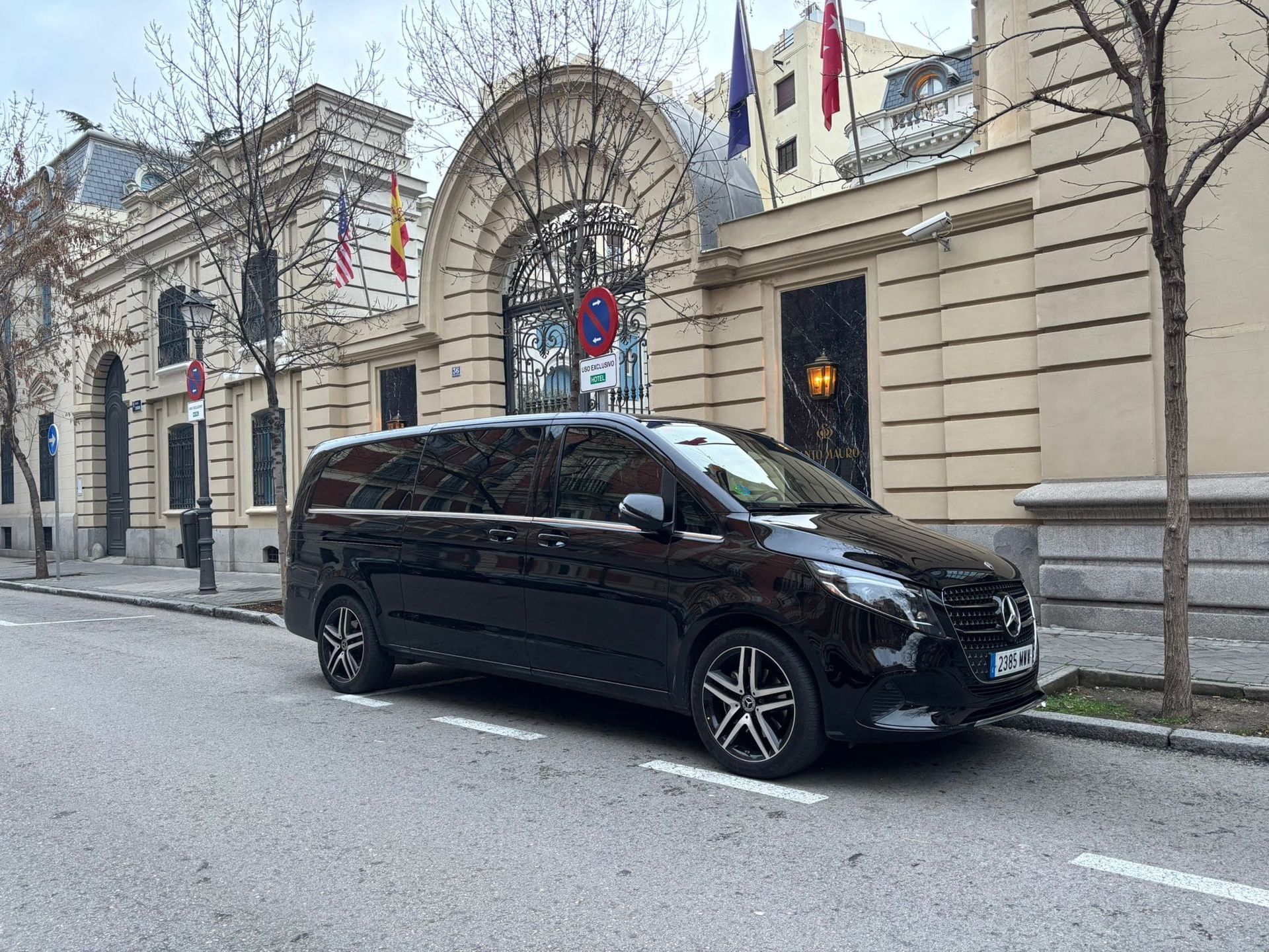 Camioneta negra estacionada frente a un edificio con entrada arqueada y banderas. Calle asfaltada.