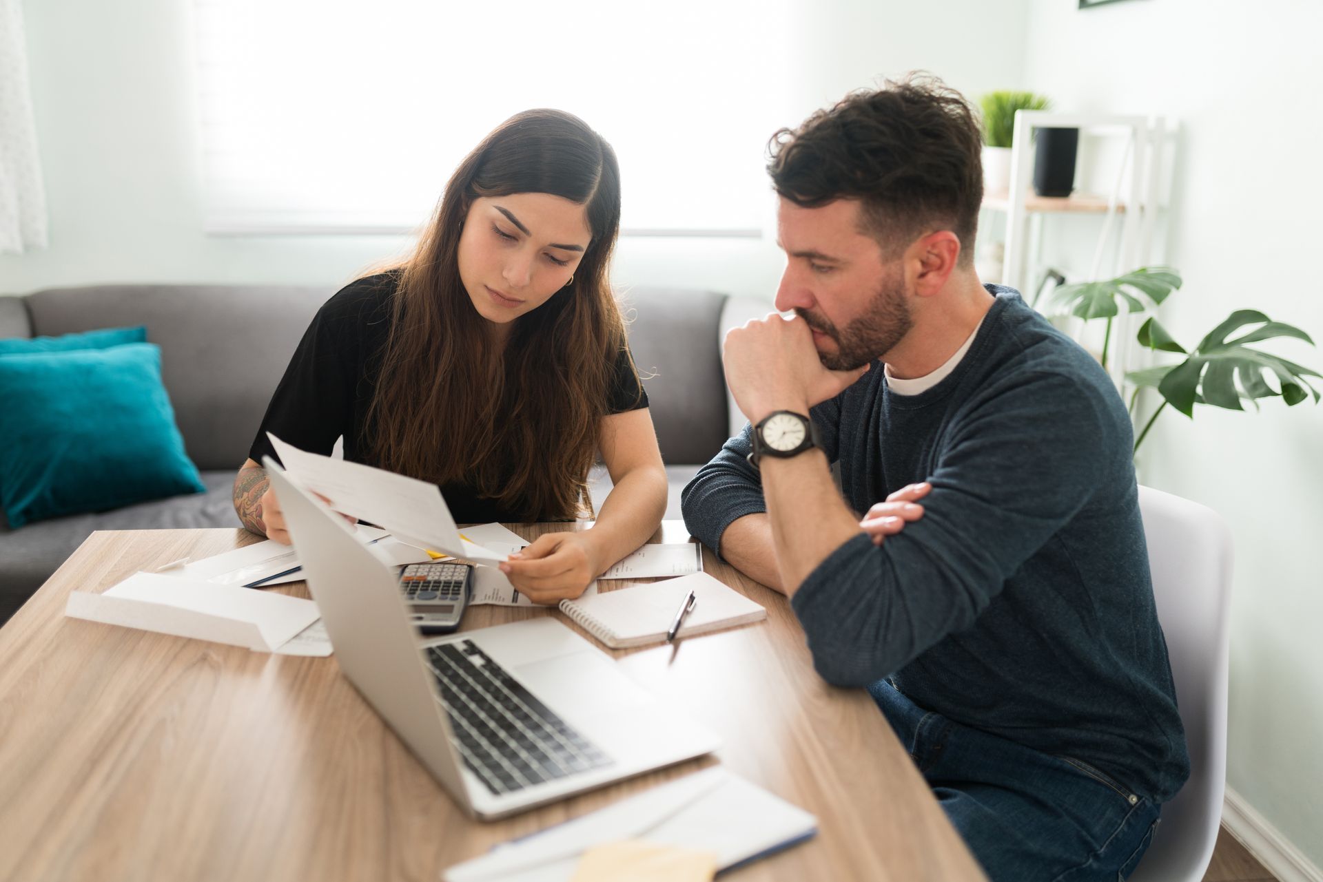 Une femme montre des documents du doigt, expliquant la situation à un homme qui regarde un ordinateur portable et réfléchit à ce qui se dit.