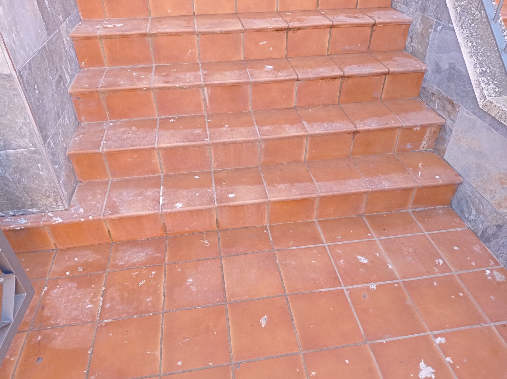 Una escalera de baldosas de terracota que conduce a un patio alicatado a juego, enmarcado por muros de piedra.