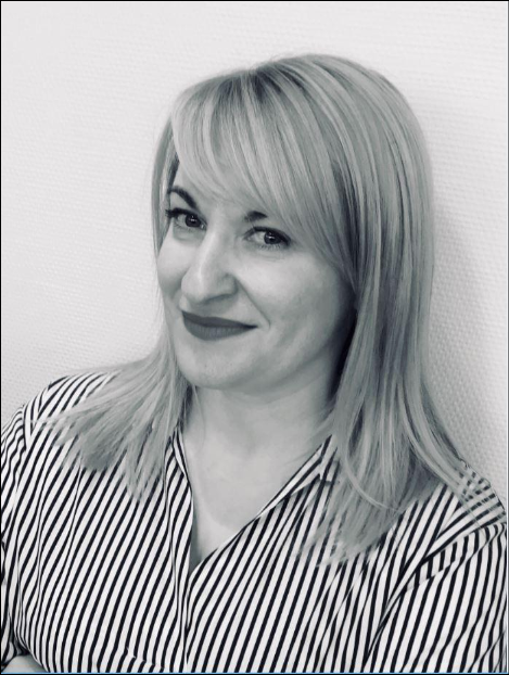 Femme blonde souriante, vêtue d'une chemise à rayures. Portrait en buste, en intérieur.