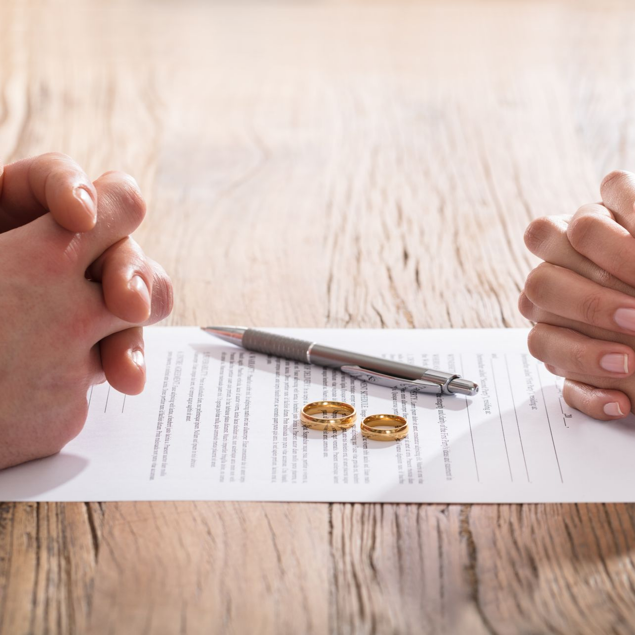 Mains jointes, alliances, stylo et papiers de divorce sur une table en bois.