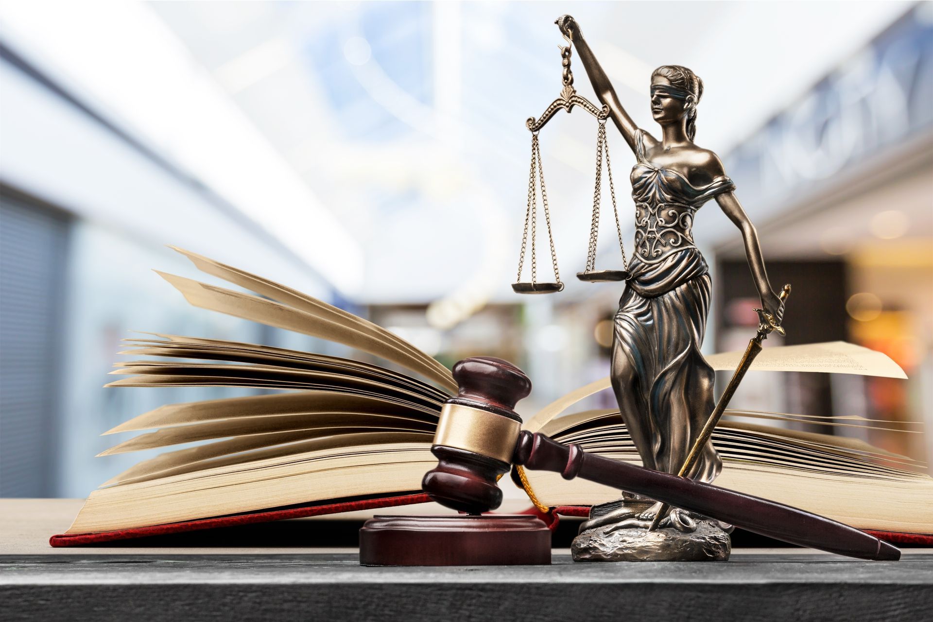 Statue de la Justice, maillet et livre de lois ouvert sur un bureau.