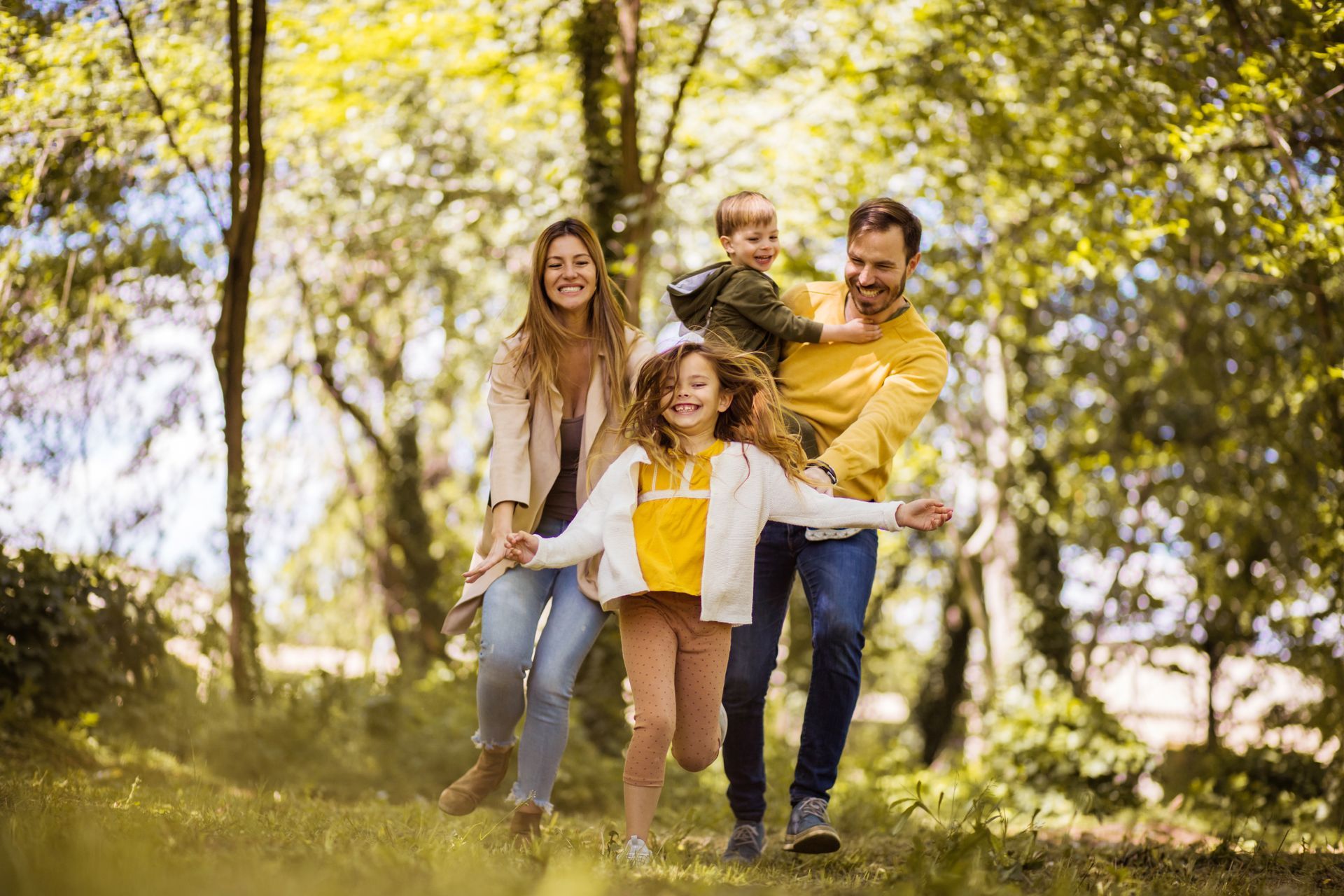 Une famille de quatre personnes rit et joue dehors, dans un parc ensoleillé.