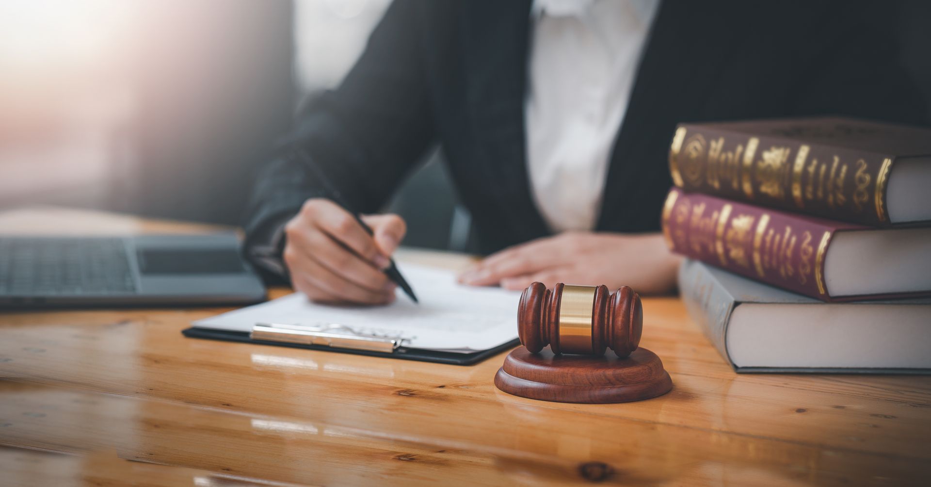 Un avocat rédigeant un document, un maillet et des ouvrages de droit posés sur un bureau en bois.