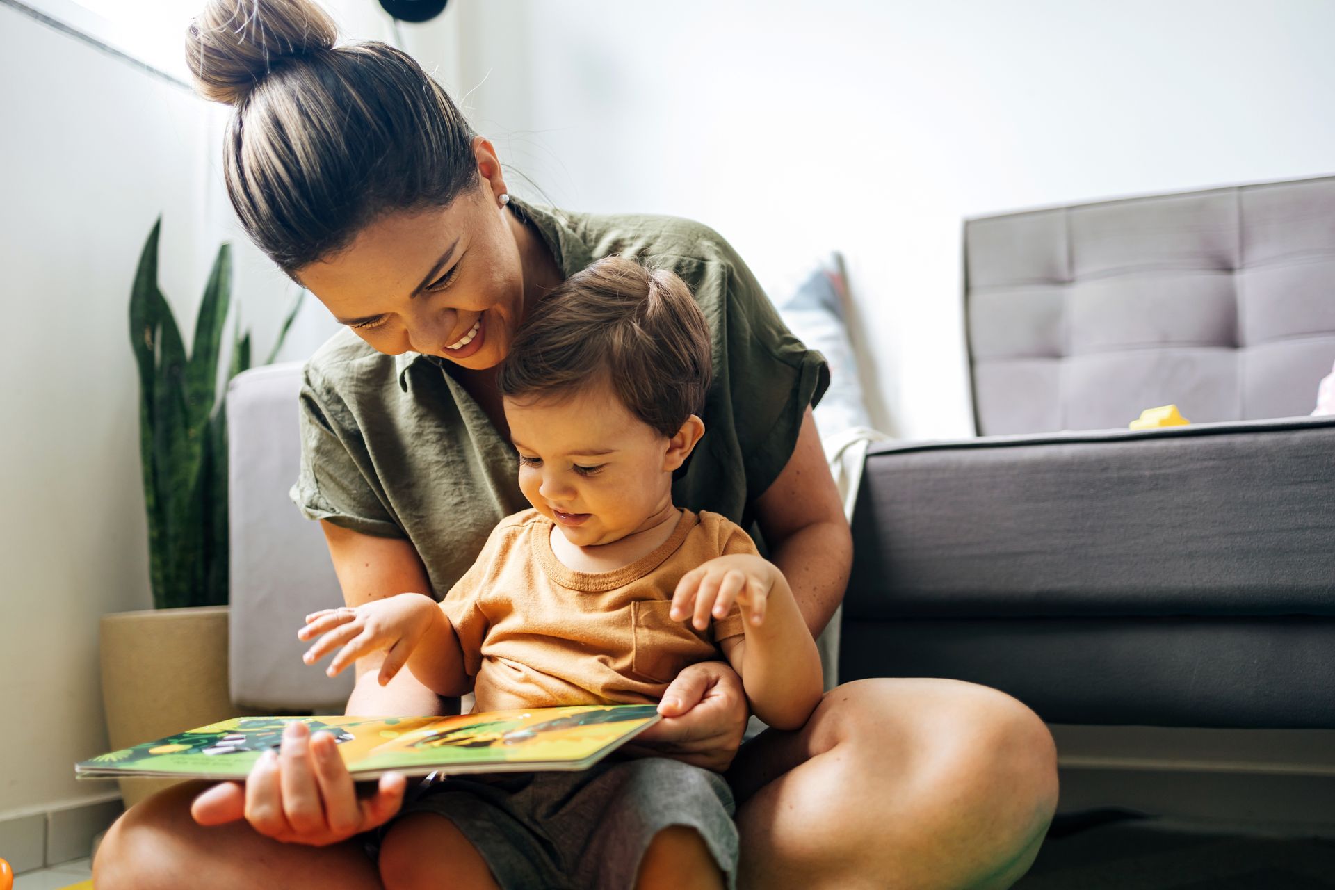 Une femme et son jeune enfant lisent un livre ensemble par terre. Tous deux sourient.